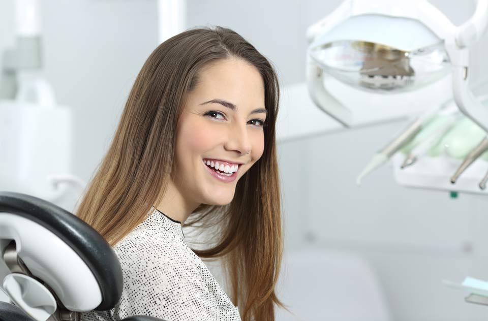 Frau sitzt in einem Zahnarztstuhl und lächelt